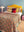 A cozy bedroom features a bed with a yellow headboard, an Ian Snow Ltd Jasmine Block Print Cotton Quilt, striped and solid pillows, pink side tables, white lamps, and a woven rug on the floor against a light blue wall.