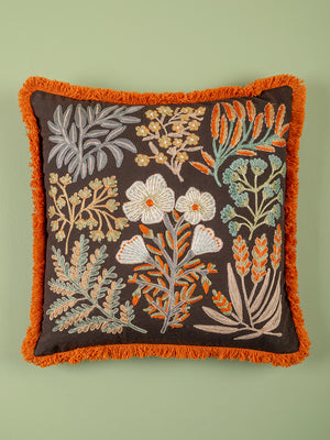 Decorative pillow with floral embroidery and orange fringe on a green background