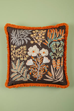 Decorative pillow with floral embroidery and orange fringe on a green background