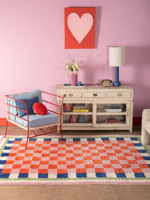 Living room with a colorful checkered rug, red chair, and pink wall with a heart-shaped painting.