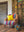 The Ian Snow Ltd Striped Velvet Armchair with a yellow pillow sits on a wooden floor beside a retro floor lamp and magazine rack, set against a rustic door and tapestry.